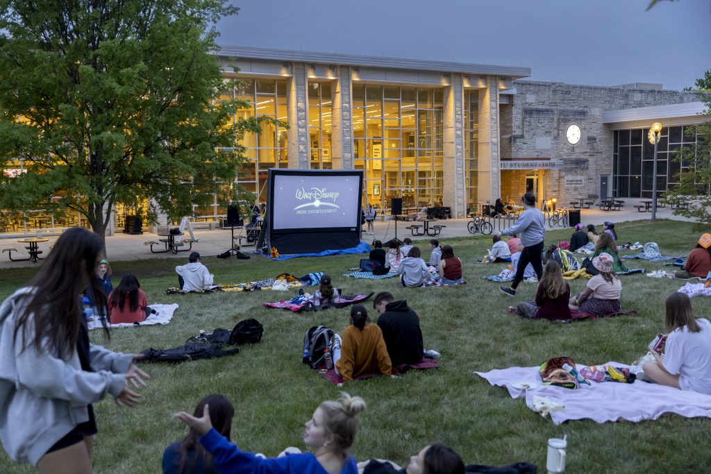 Students lounge in the grass outside the student center for a movie night,